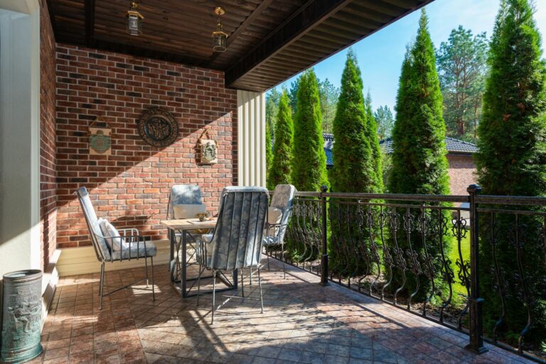 A cozy outdoor patio with comfortable seating, brick walls, and lush greenery.