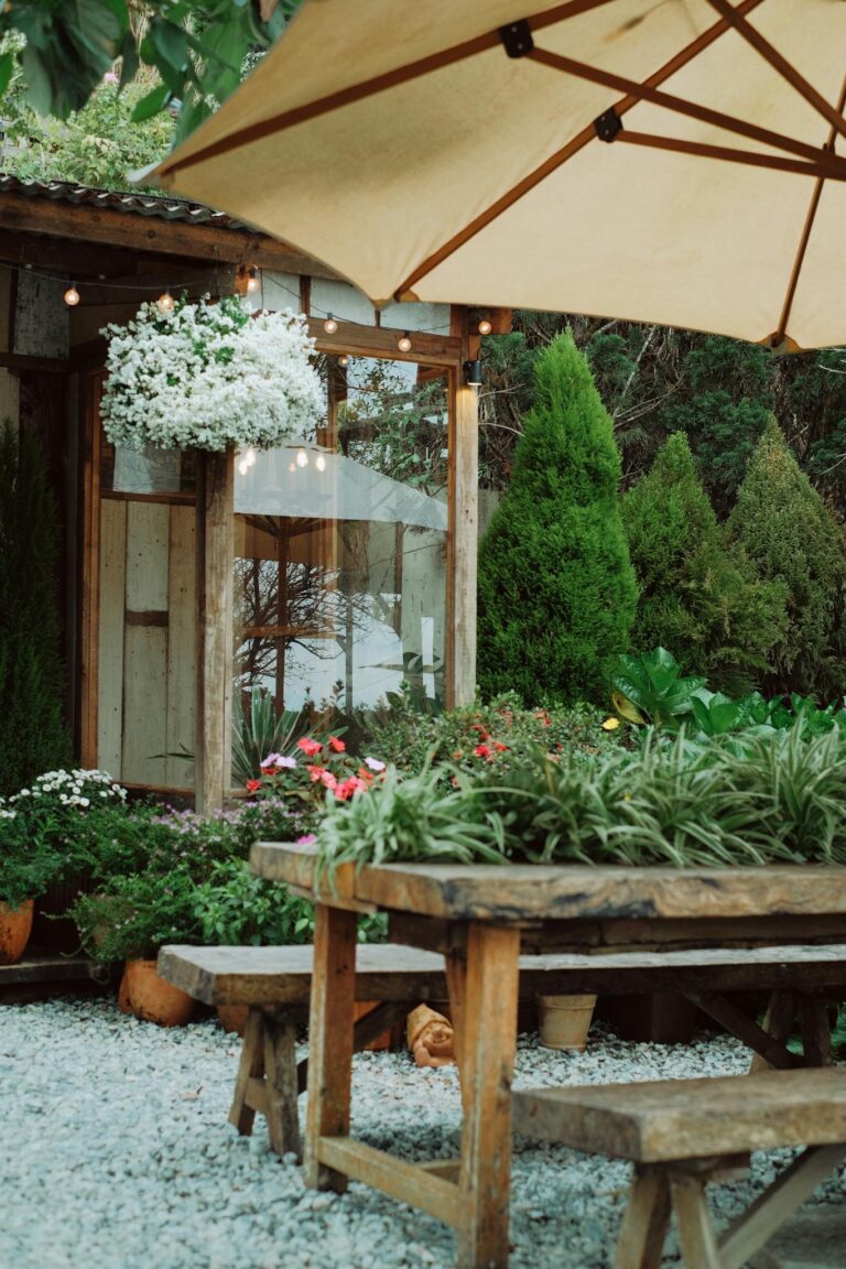 Charming rustic garden patio with wooden furniture, vibrant flowers, and large umbrella.