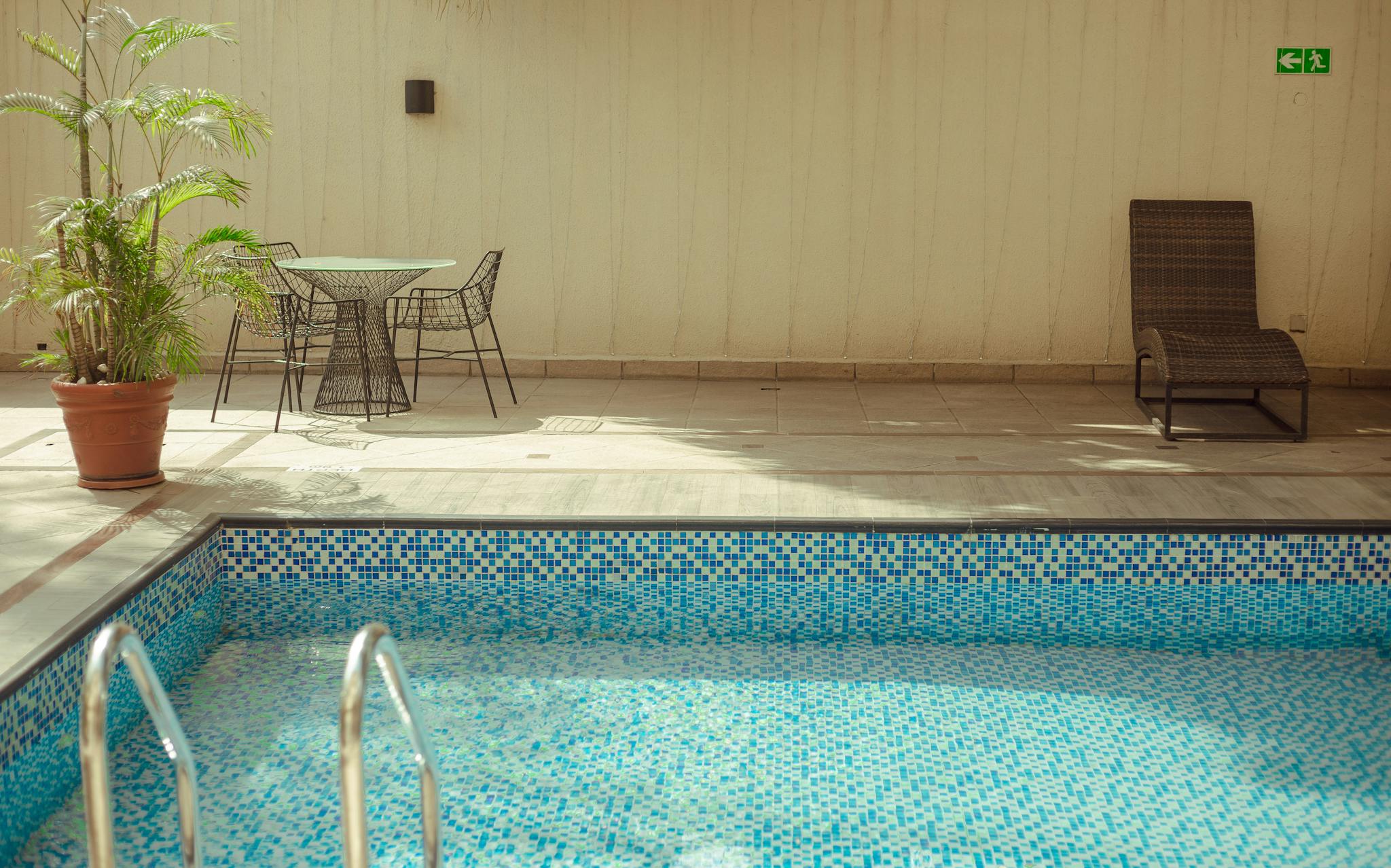 Relaxing poolside area with a lounge chair, plants, and table under natural sunlight.